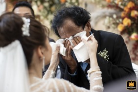 At W Bangkok, the father of the bride wipes his eyes with a kerchief, visibly moved, as the bride gently adds two more tissues to help, highlighting the deep bond and shared emotions of the day.
